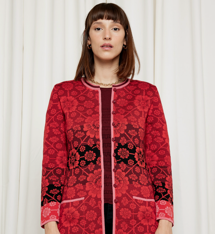 Woman wearing a red floral jacket against a light curtain backdrop