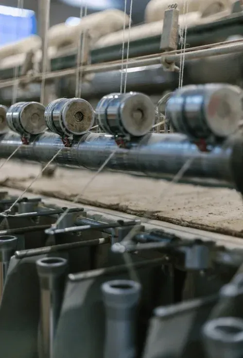 Close-up of textile machinery threading yarn through spindles in a factory.