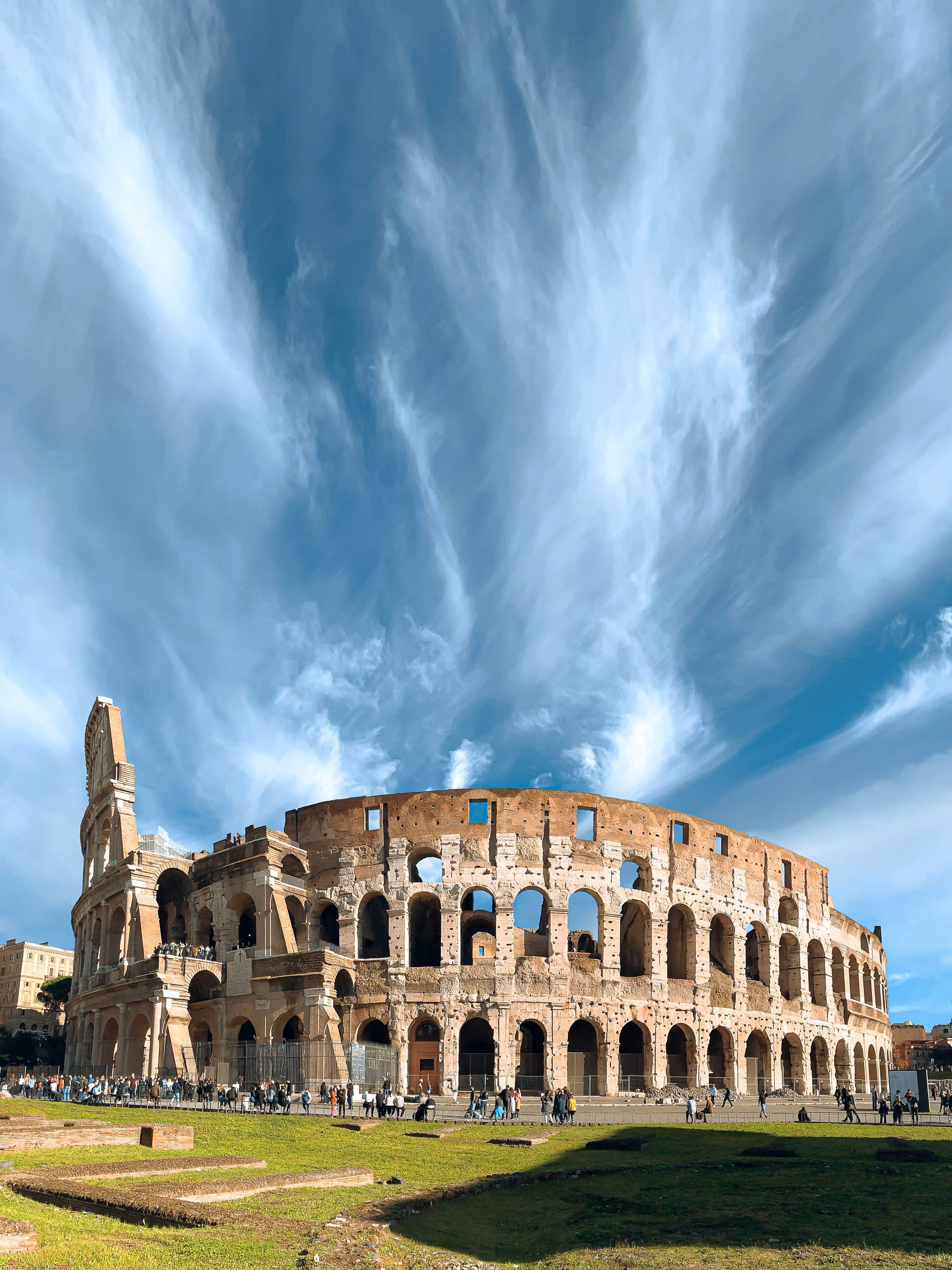 The Colosseum in Rome under a dramatic blue sky, with a grassy foreground
