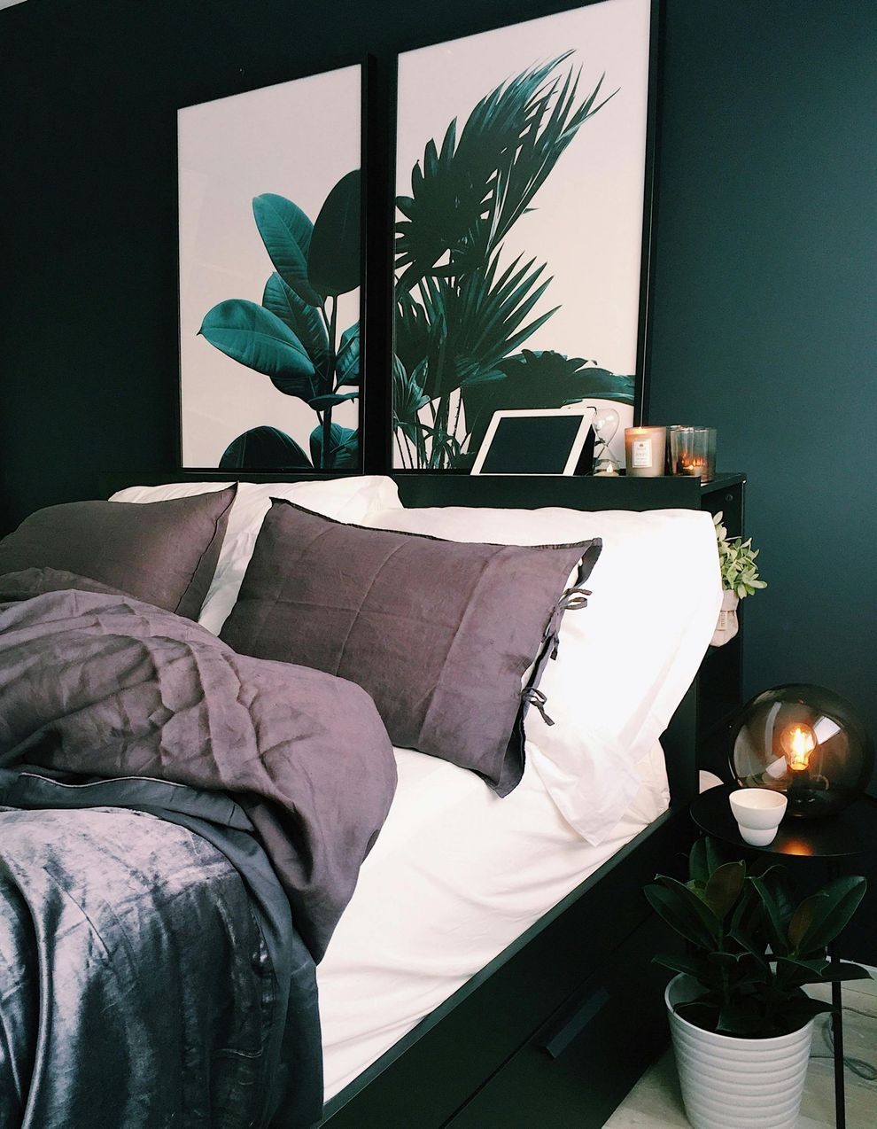 Bedroom with a dark teal wall and bed. Two large botanical art prints hang above the headboard.