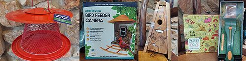 A bird feeder , a birdhouse , and a camera are sitting on a table.