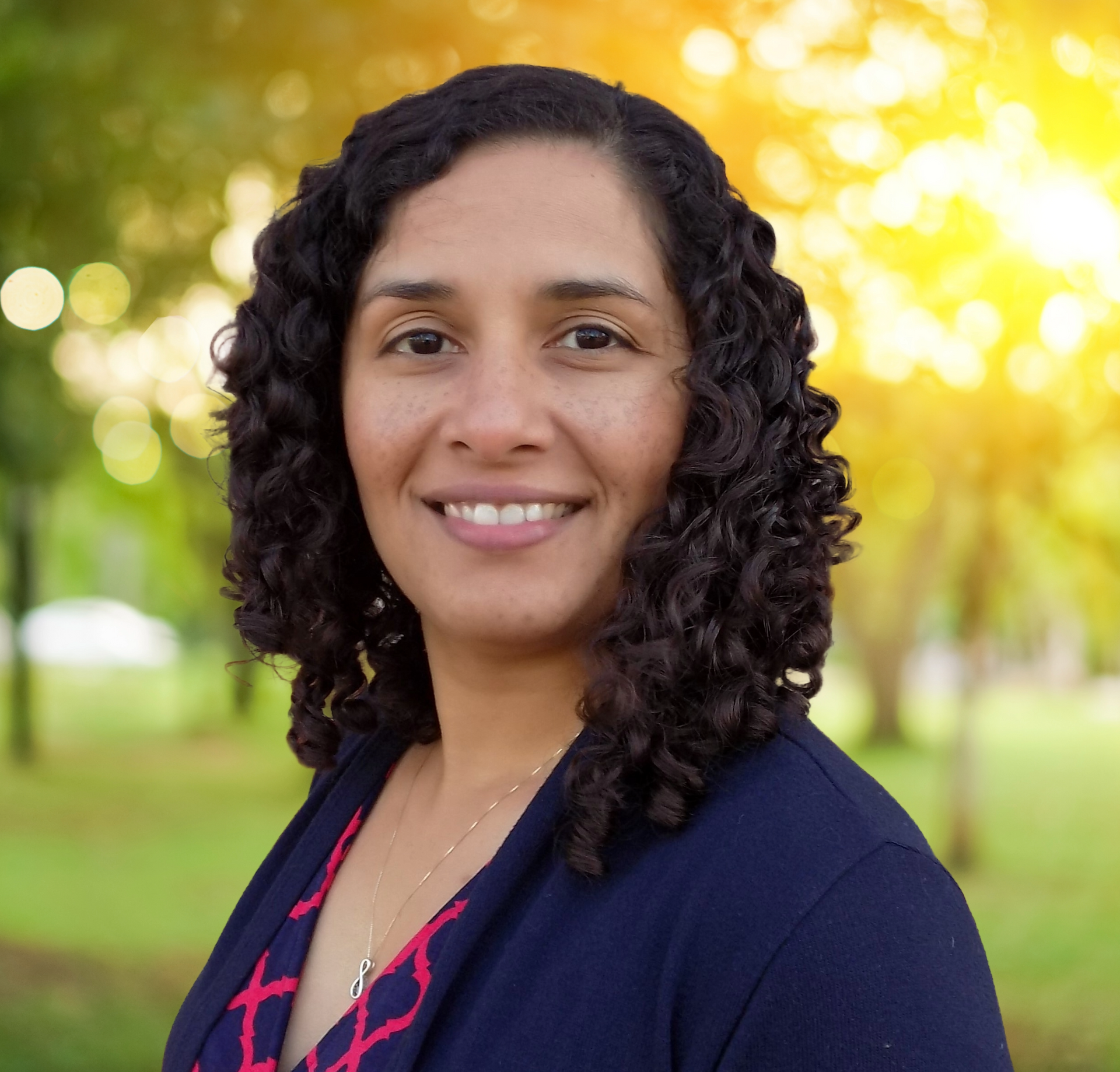 A woman with curly hair is smiling in front of a brick wall
