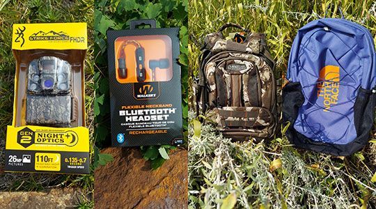 A backpack , headphones , and a camera are sitting in the grass.