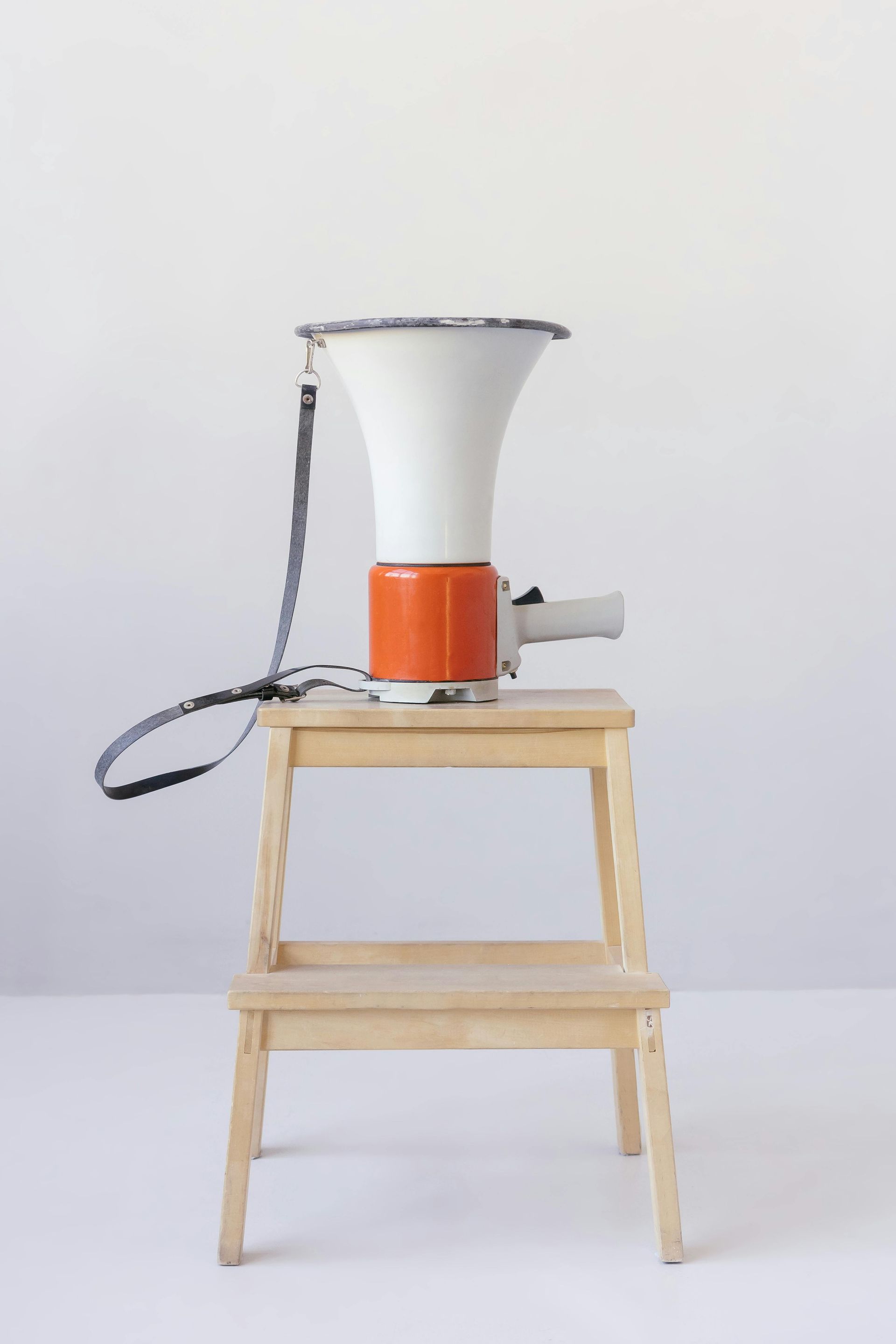 A white and orange megaphone is sitting on a wooden stool.