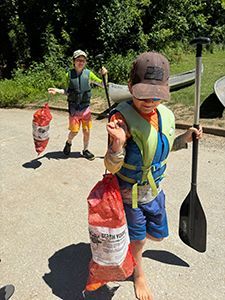 A young boy is holding a paddle and a bag of trash.