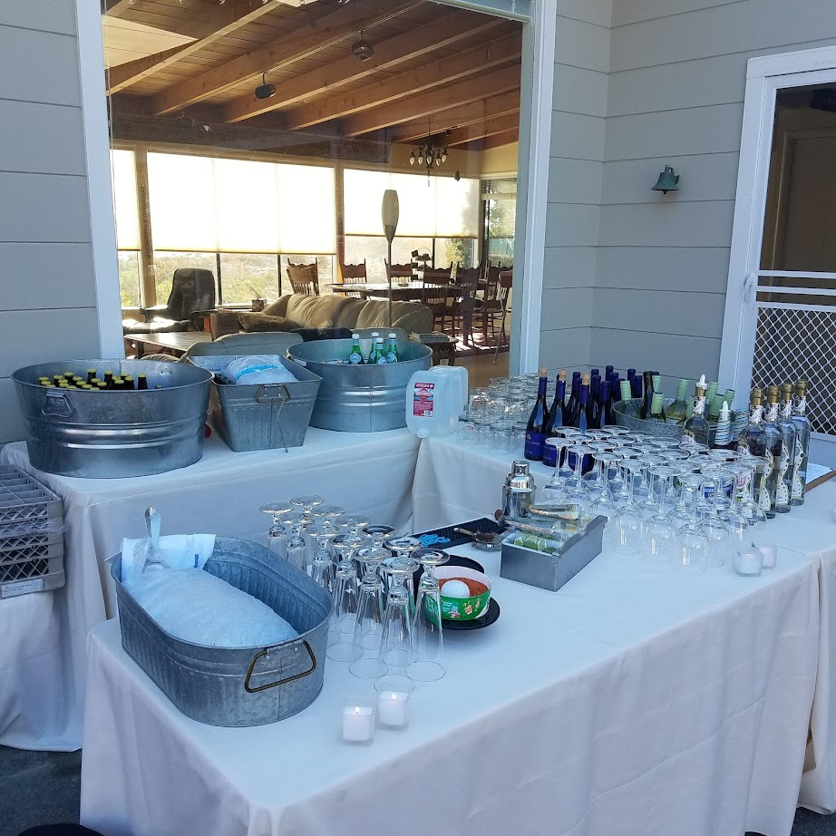 White horse trailer converted to a bar, lit up at night. Wooden barrels and drink dispensers are in front.