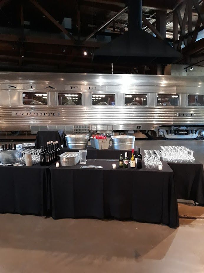 Bar setup with drinks in front of a silver train car in a dimly lit industrial space.