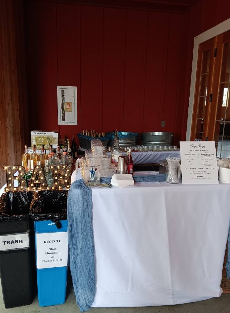 Bar setup with drinks, trash cans, and a sign on a red-walled patio.