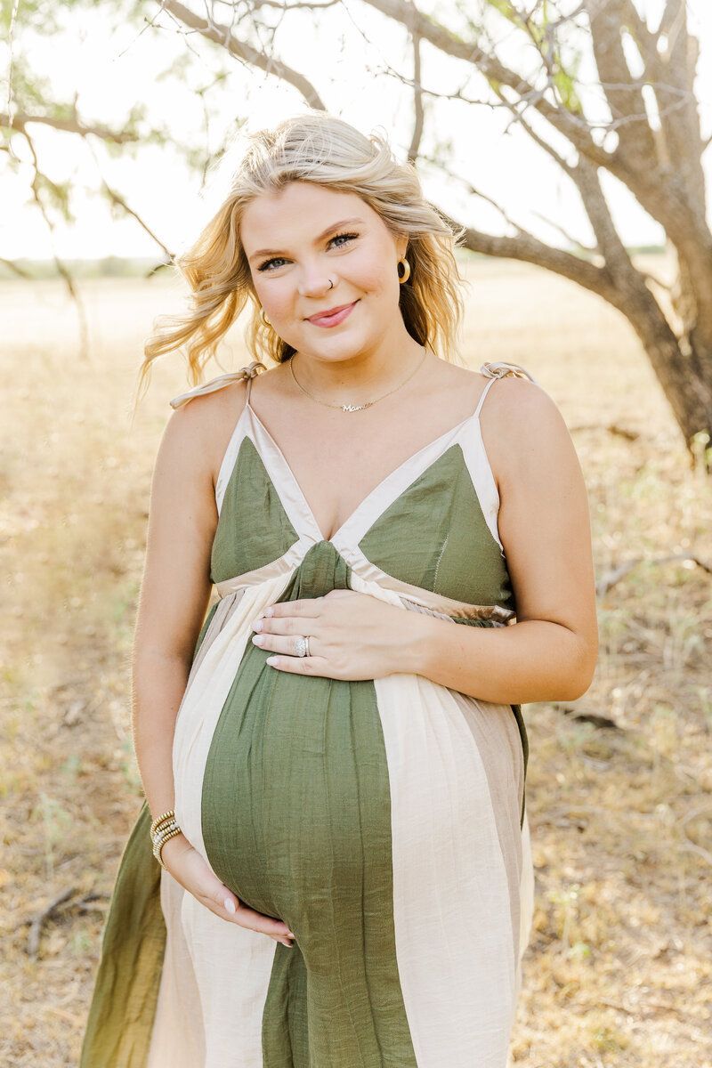 A pregnant woman in a green and white dress is holding her belly.