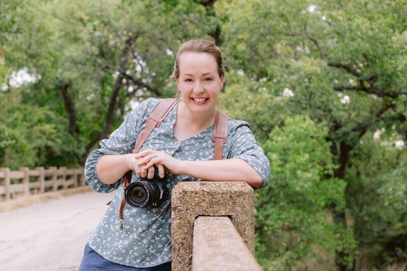 A woman is leaning on a railing holding a camera.