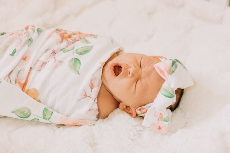 A newborn baby is wrapped in a blanket and wearing a headband.