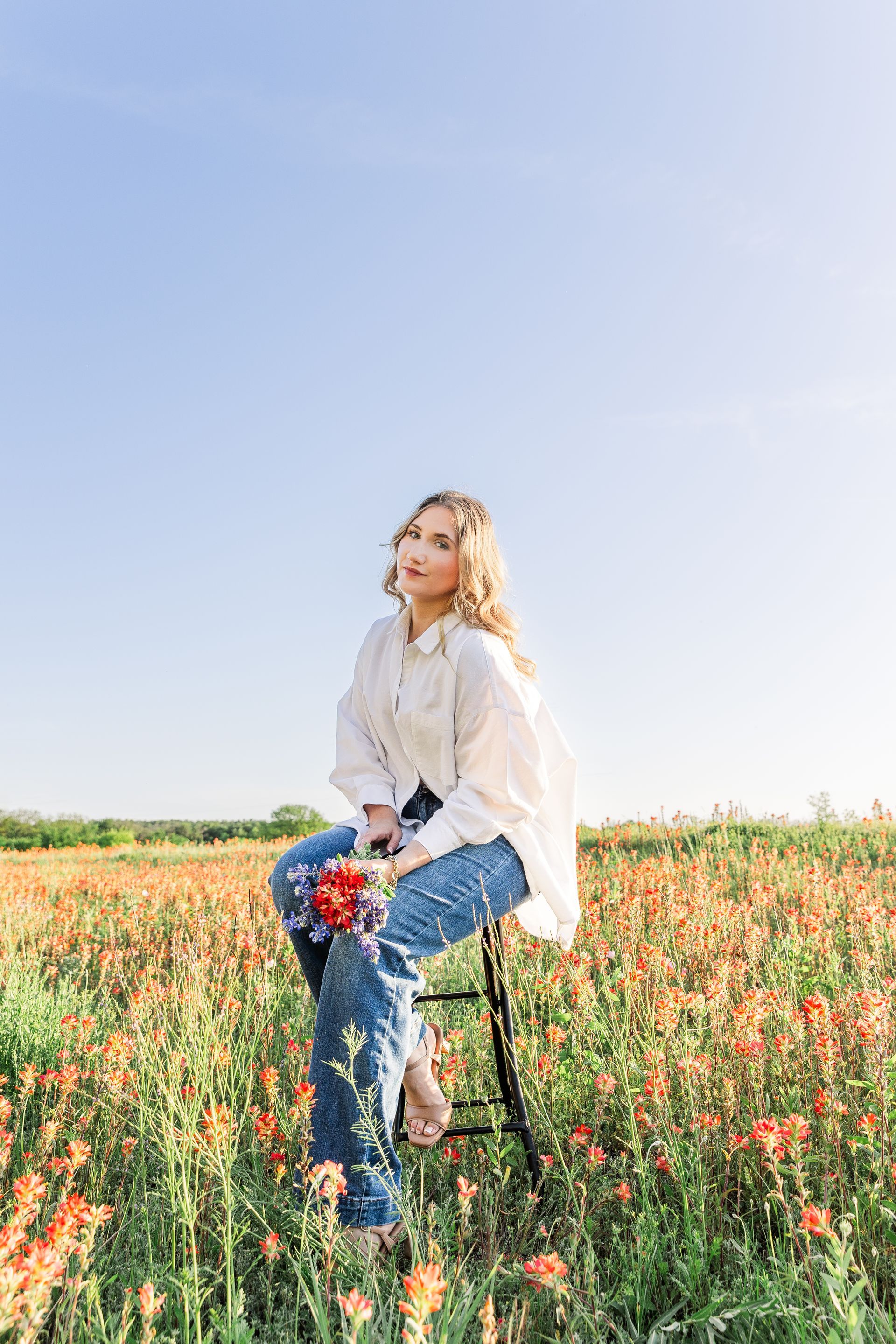 A woman is sitting on a stool in a field of flowers.
