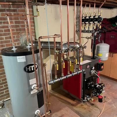 A hot water heater is in a basement next to a boiler