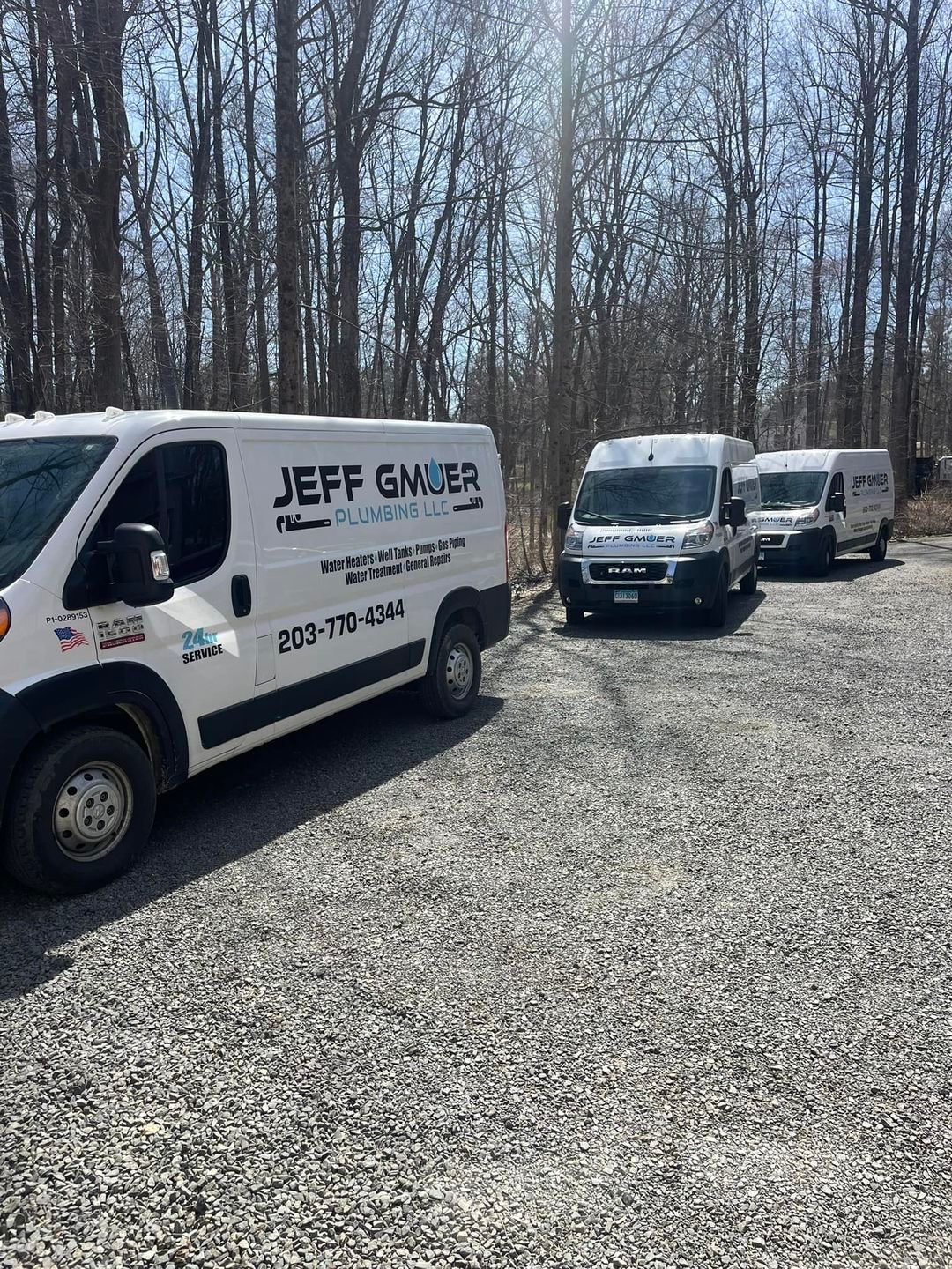 A row of white Jeff Gmuer Plumbing vans parked in a gravel lot.