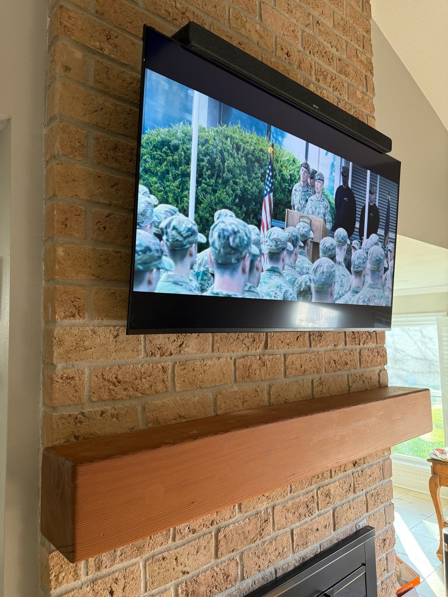 A flat-screen television mounted on a textured brick fireplace wall above a thick, wooden mantel.