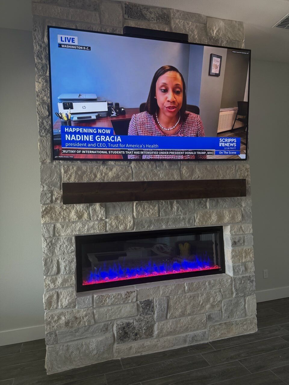 A flat screen tv is mounted on a stone wall above a fireplace.