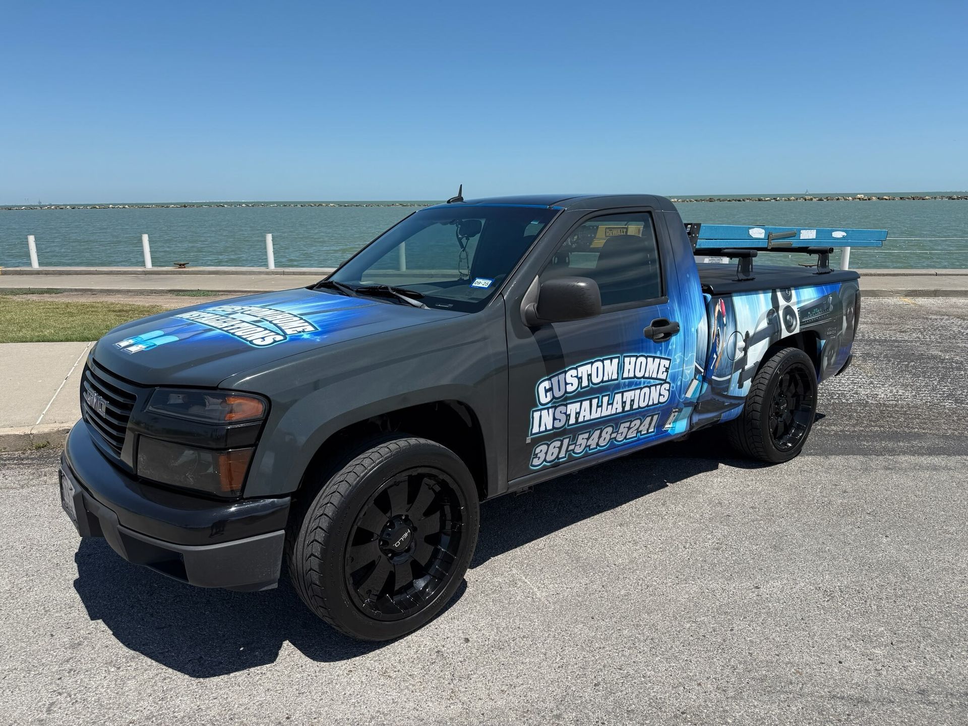 A truck is parked on the side of the road in front of a body of water.