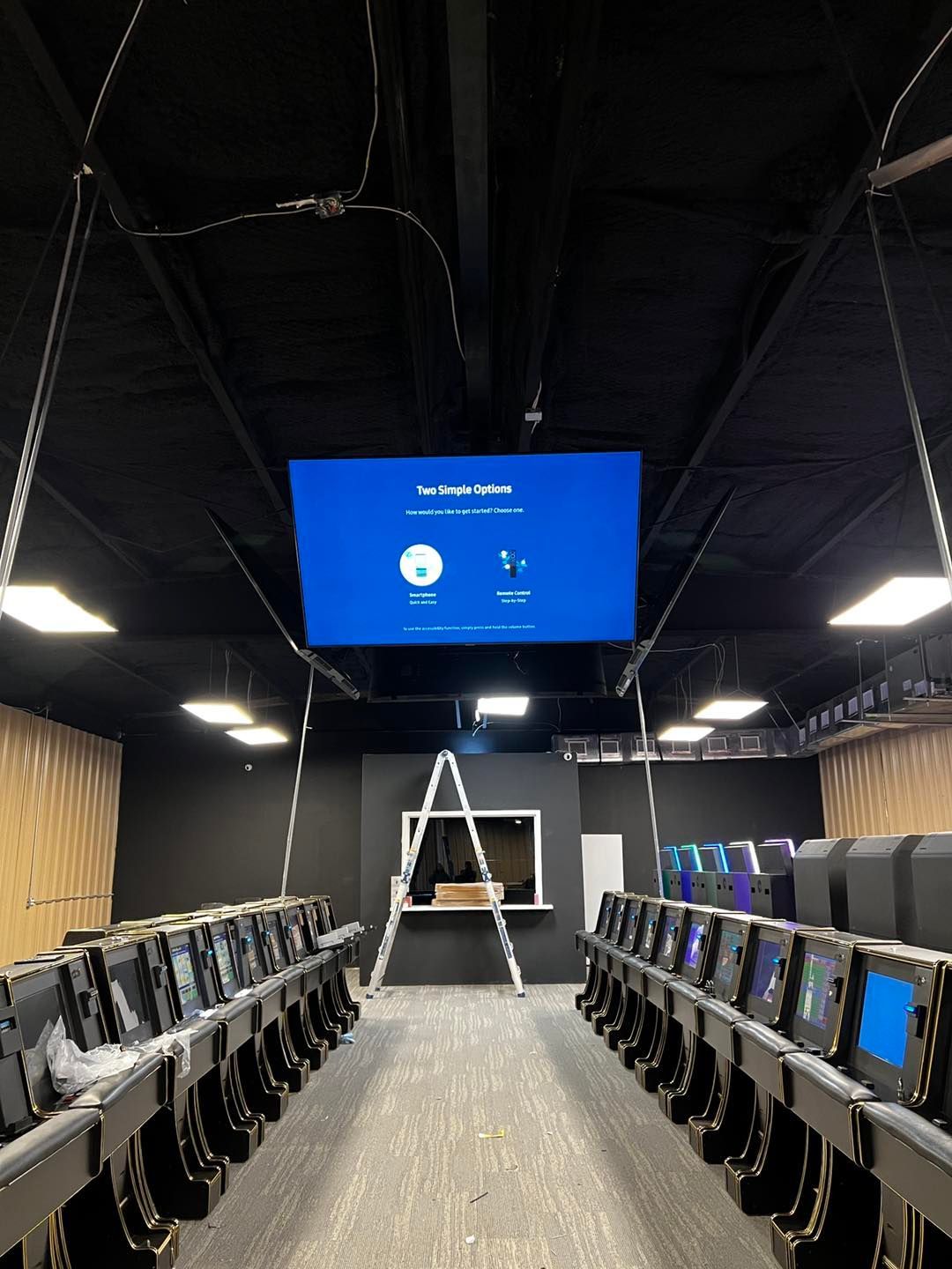 A large screen is hanging from the ceiling of a computer lab.