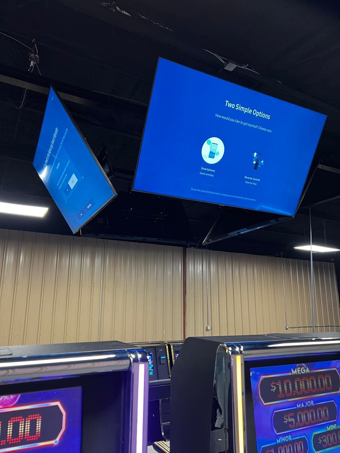 A computer monitor is hanging from the ceiling above a slot machine.