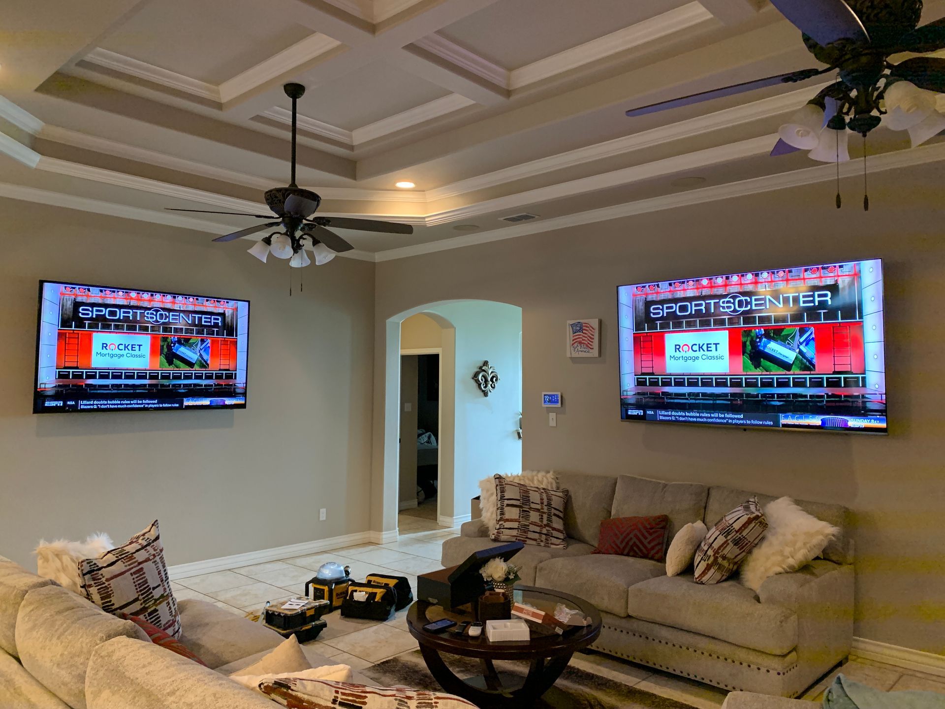 A living room with two flat screen tvs on the wall and a ceiling fan.