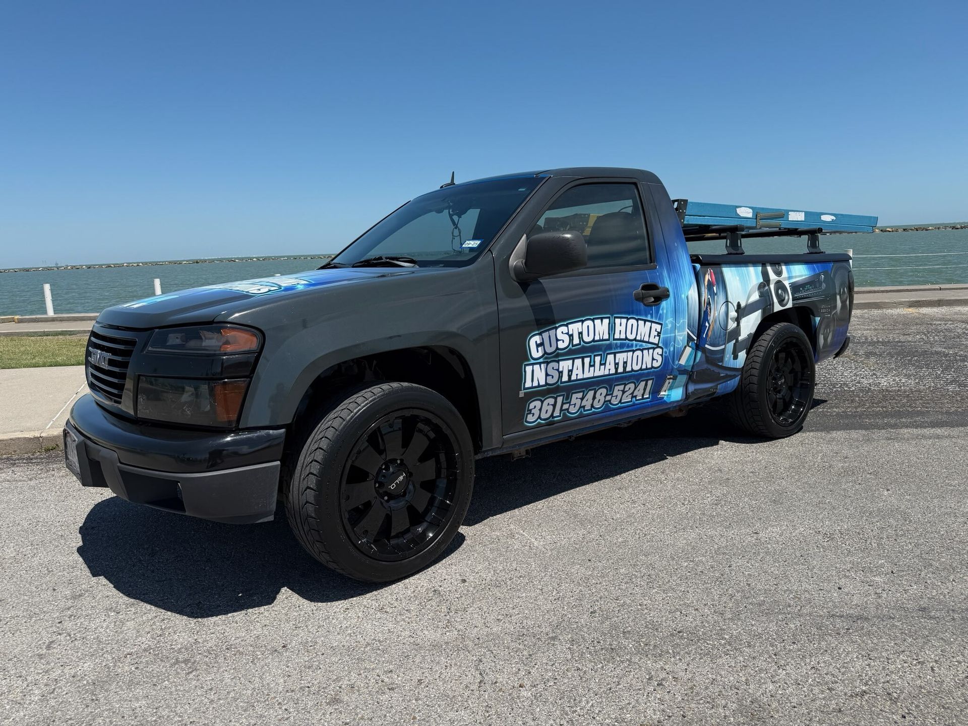 A truck is parked on the side of the road in front of a body of water.