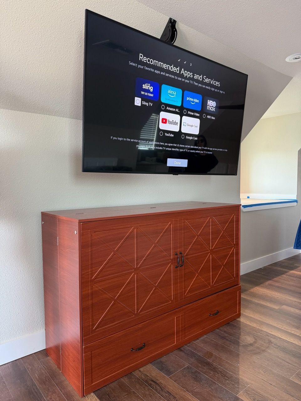 Wall-mounted TV above a reddish-brown cabinet in a room with hardwood floors and an angled ceiling.