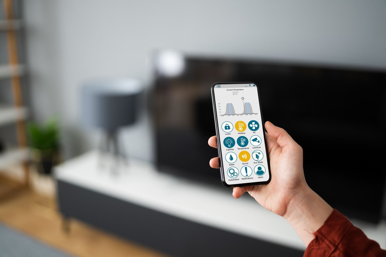 Person holding smartphone displaying smart home app; living room background.