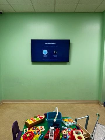A room with a table and chairs and a television on the wall.