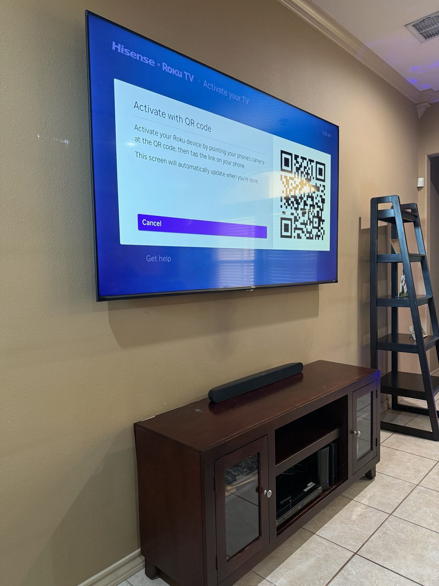 Large TV mounted on beige wall, above a dark wood media console and soundbar. Black step ladder in background.
