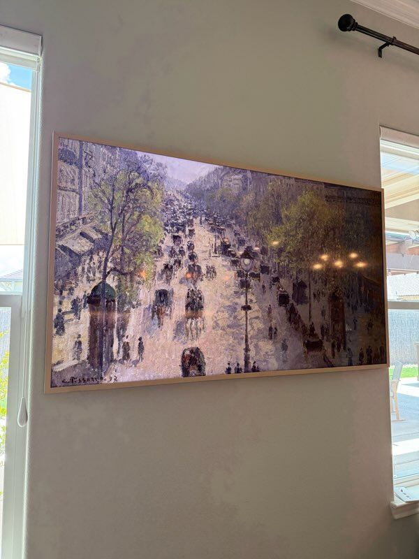 A large painting is hanging on a wall next to a window.