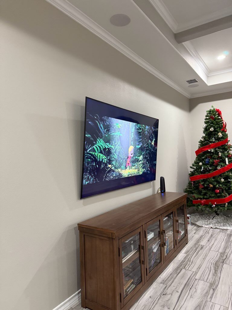 TV on wall above wooden console in room, Christmas tree in background.