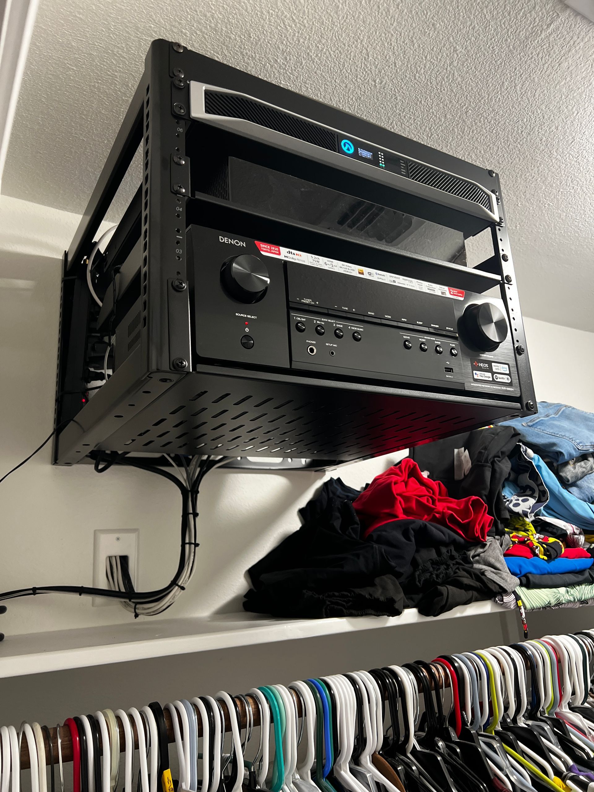 A closet with clothes hanging on a shelf and a receiver mounted to the ceiling.