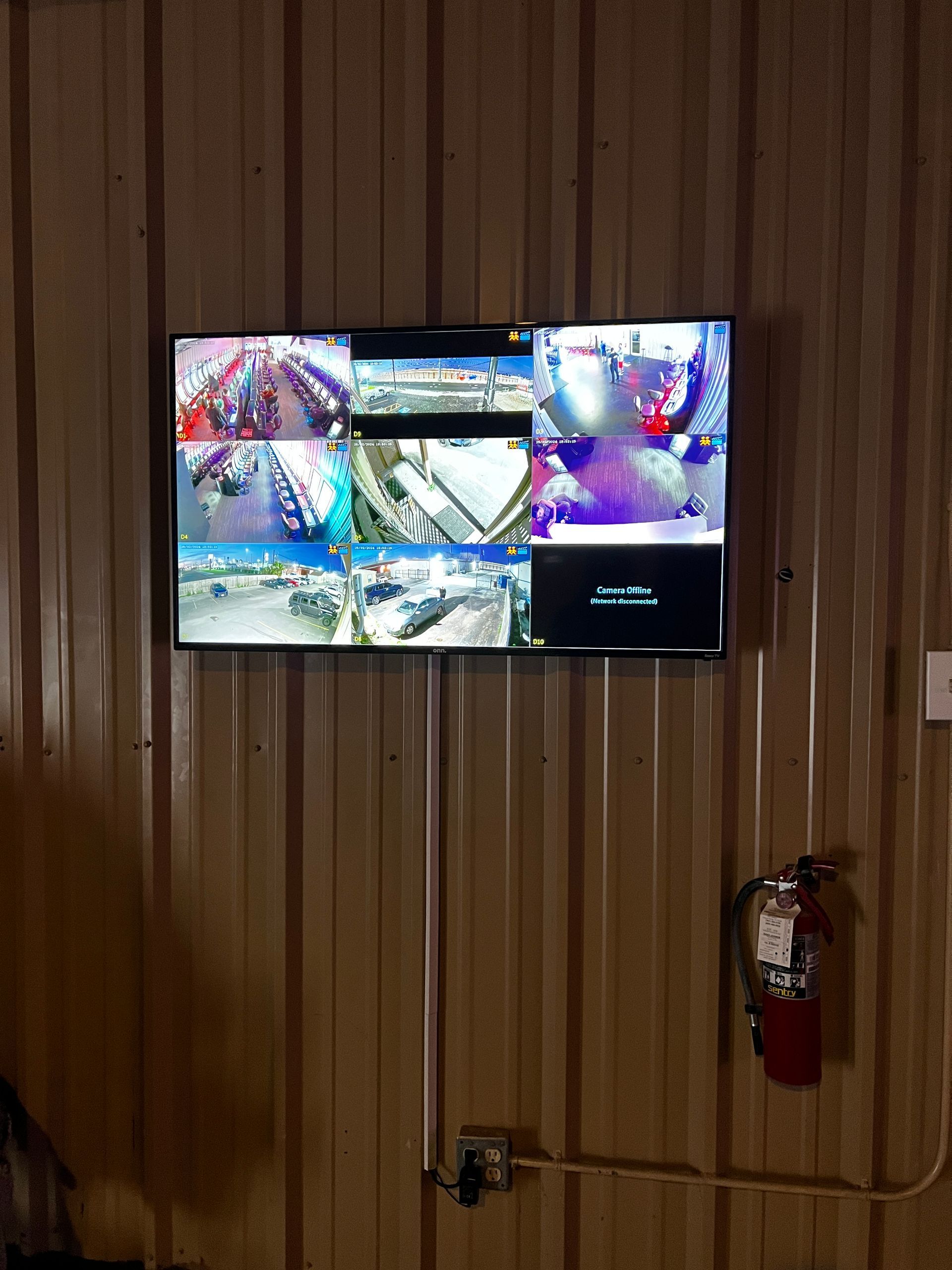 A television is hanging on a wall with a fire extinguisher next to it.