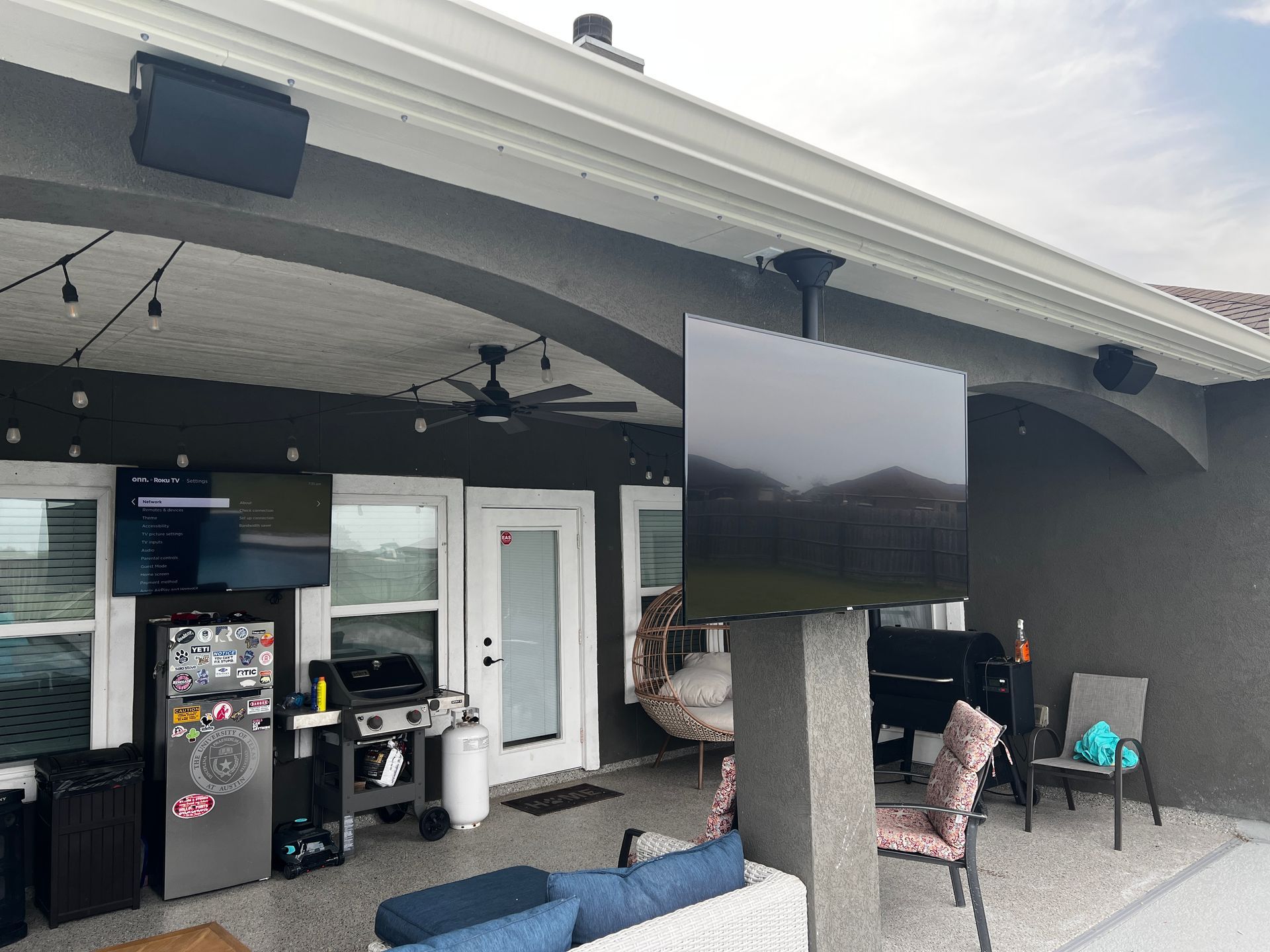 A patio with a couch , chairs , a grill and a flat screen tv.