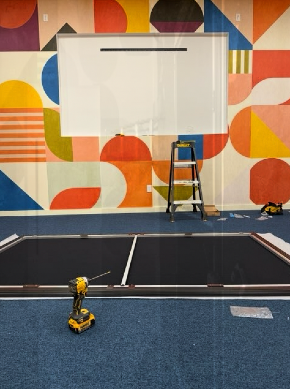 A drill sits on the floor in front of a colorful wall