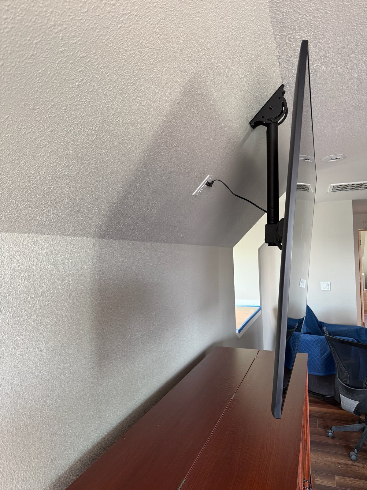 A large, black television mounted on a black arm over a wooden cabinet against a white wall and sloped ceiling.