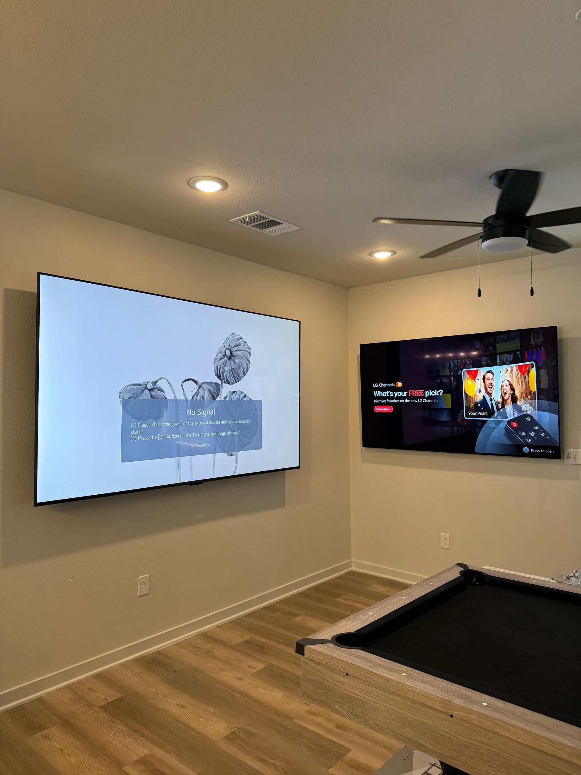 A media room with a pool table, two TVs on the wall, one displaying a cartoon and the other a video game.