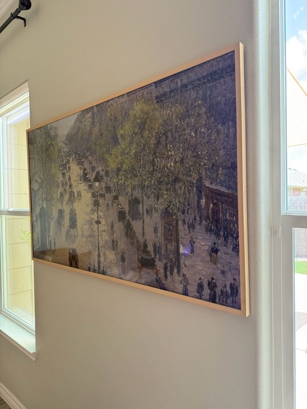 A large painting is hanging on a wall next to a window.