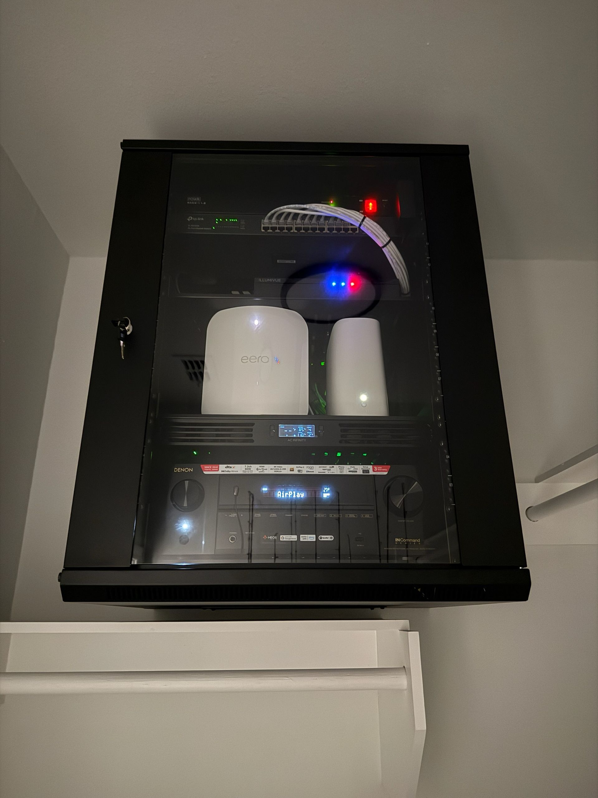 Black network rack with electronic equipment mounted on a wall.