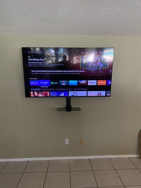 A large TV mounted on a beige wall, displaying a streaming service interface.  A light switch and tiled floor are below.