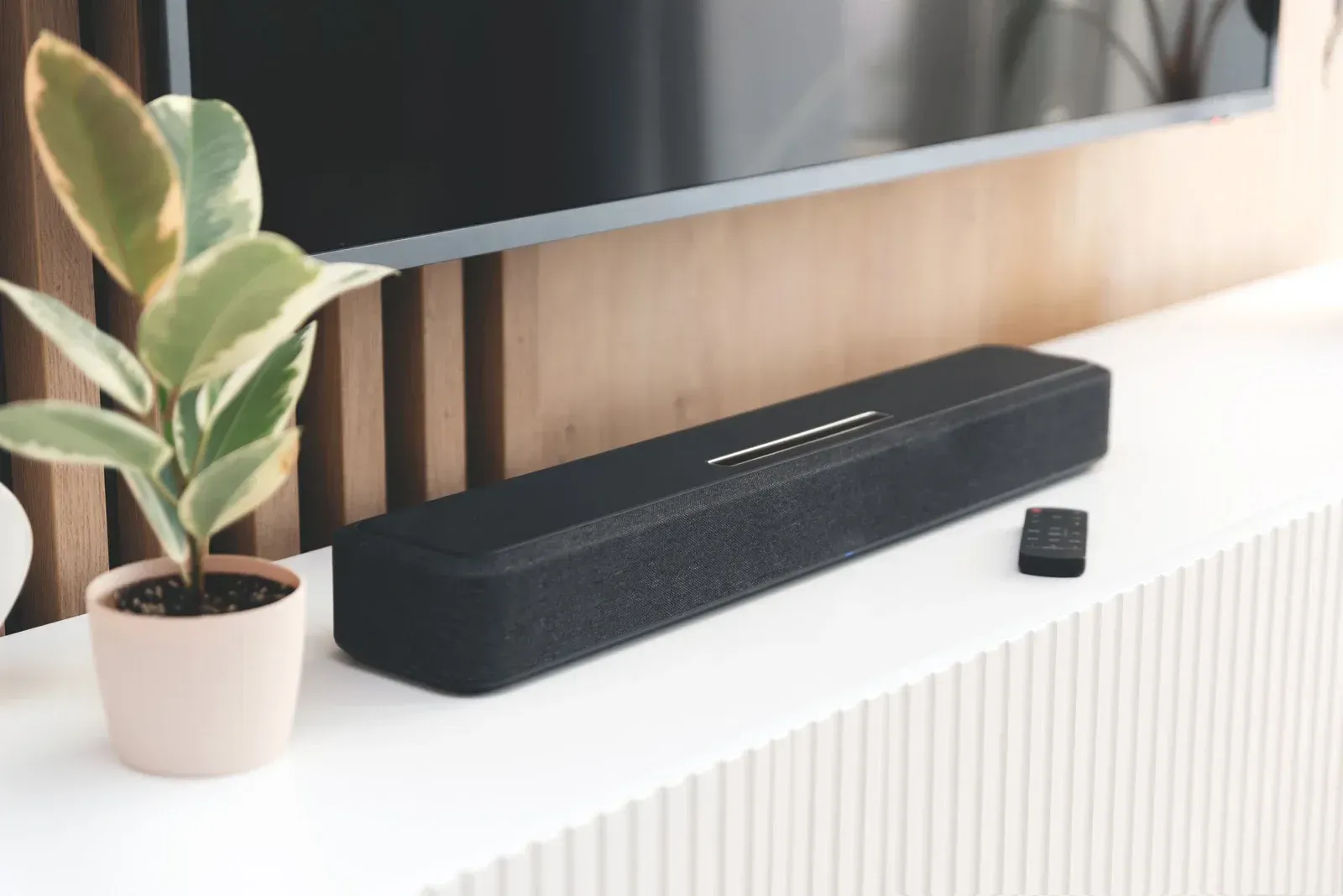 A sound bar is sitting on a shelf next to a potted plant.