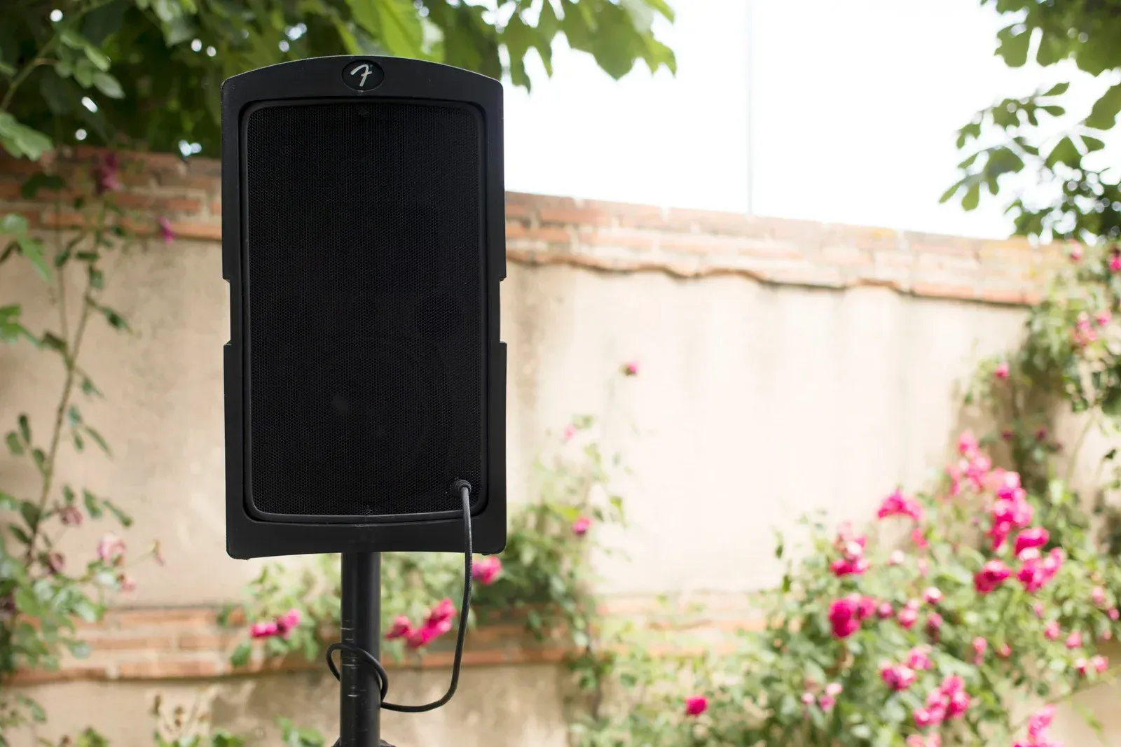 A speaker is sitting on a stand in front of a fence and flowers.