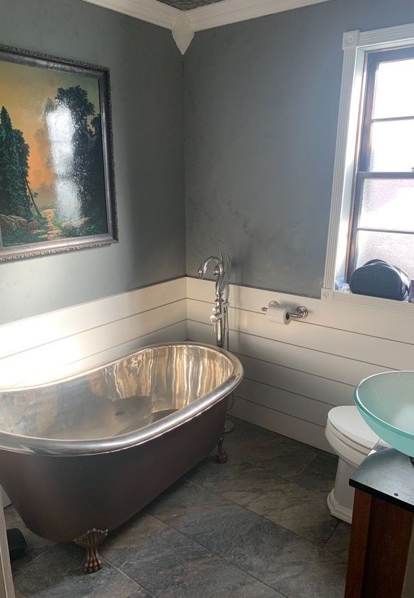 A bathroom with a bathtub , toilet , sink and a painting on the wall.