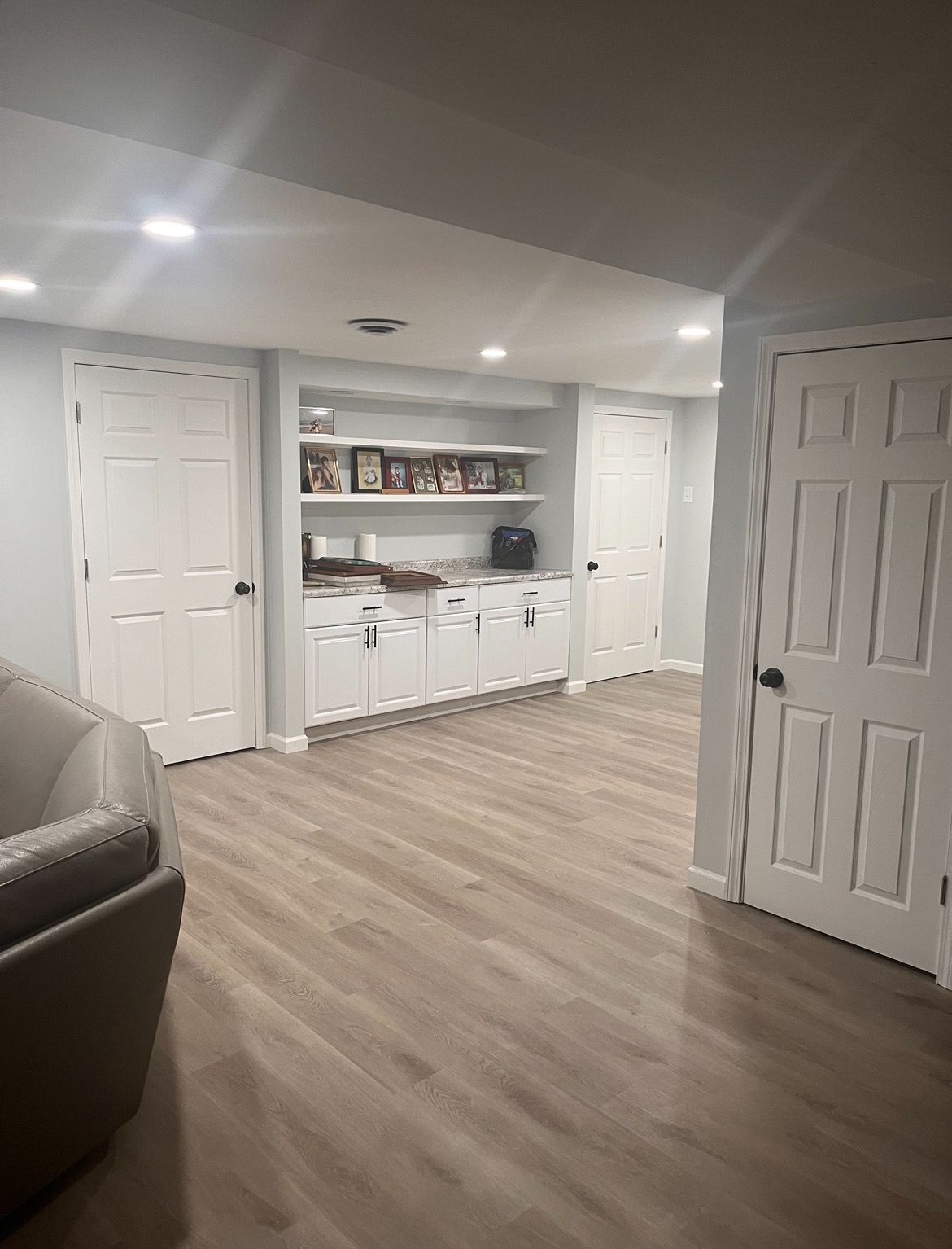 A living room in a basement with hardwood floors and white cabinets.