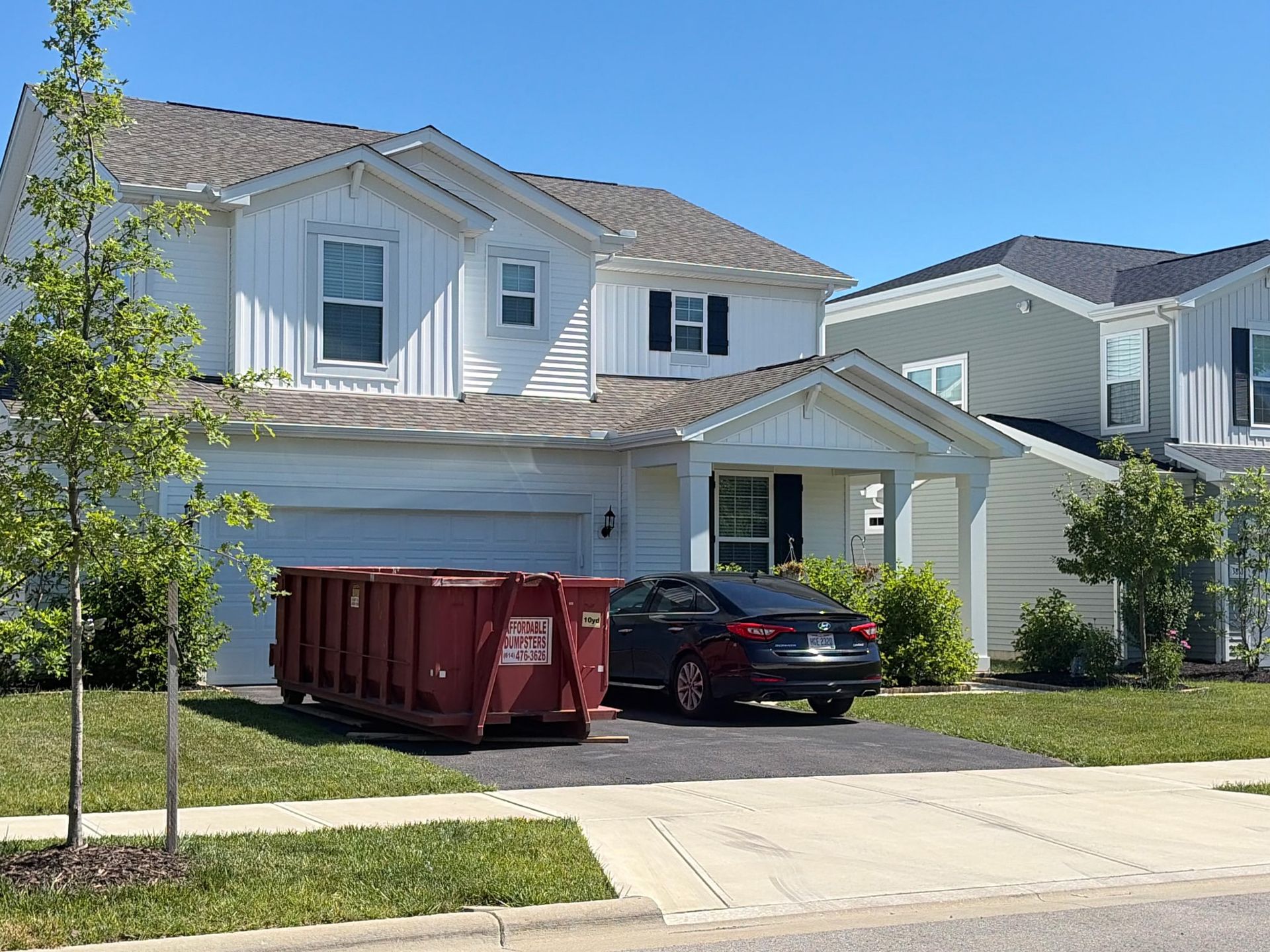 Suburban two-story house with a red dumpster and black car parked in the driveway. Suburban two-story house with a red dumpster and black car parked in the driveway.