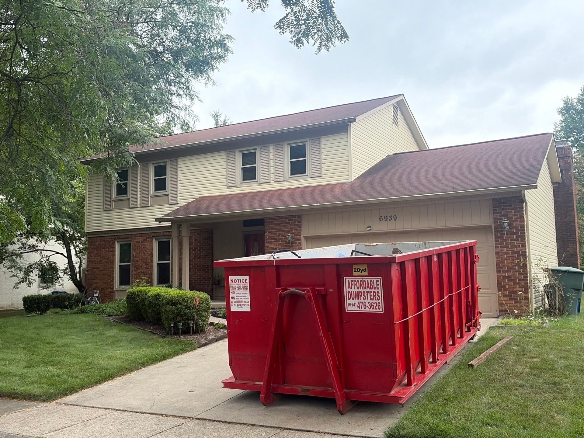 Red dumpster in front of a two-story house with driveway and lawnRed dumpster in front of a two-story house with driveway and lawn Red dumpster in front of a two-story house with driveway and lawn