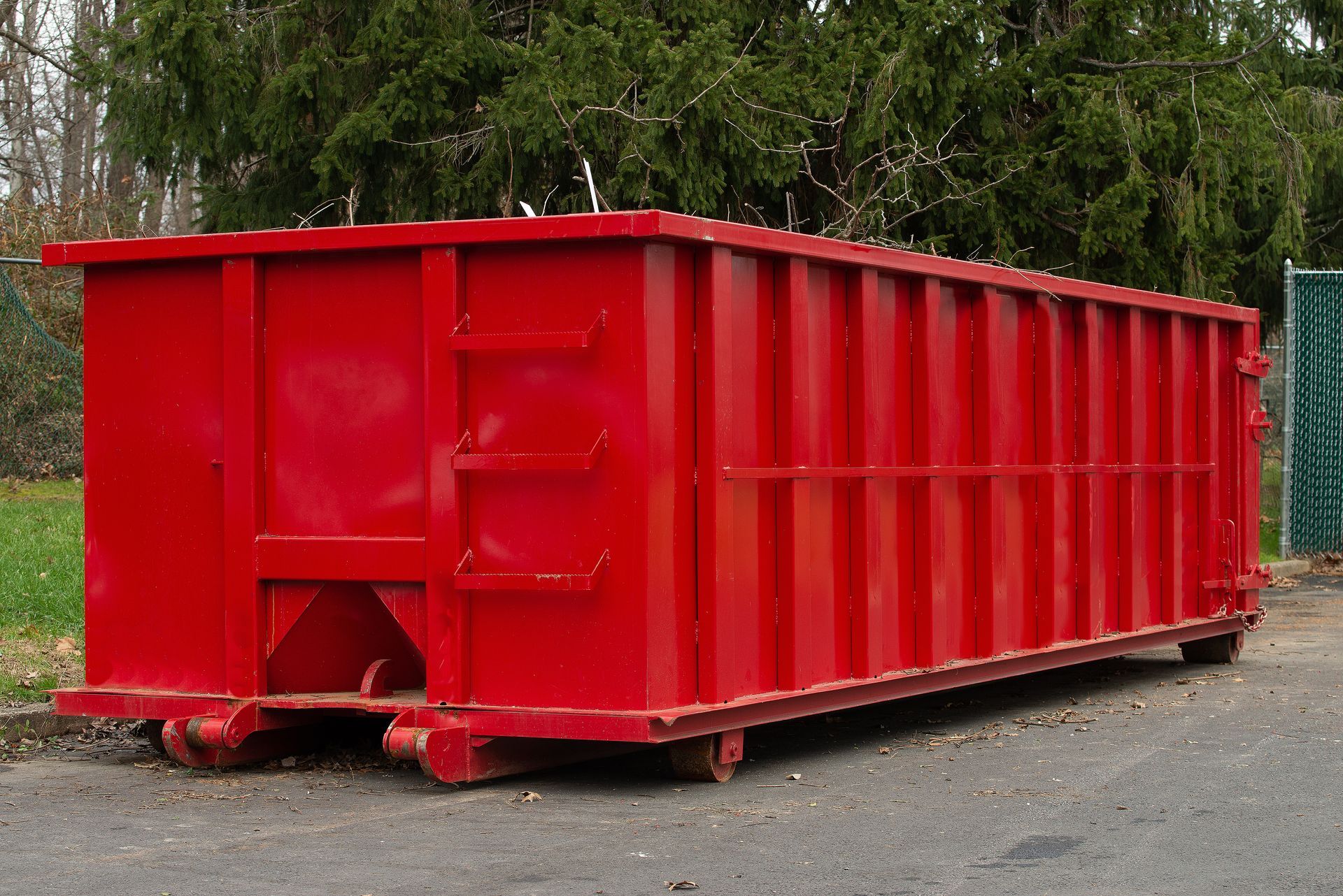 Red construction dumpster on a gravel roadside with trees in the background