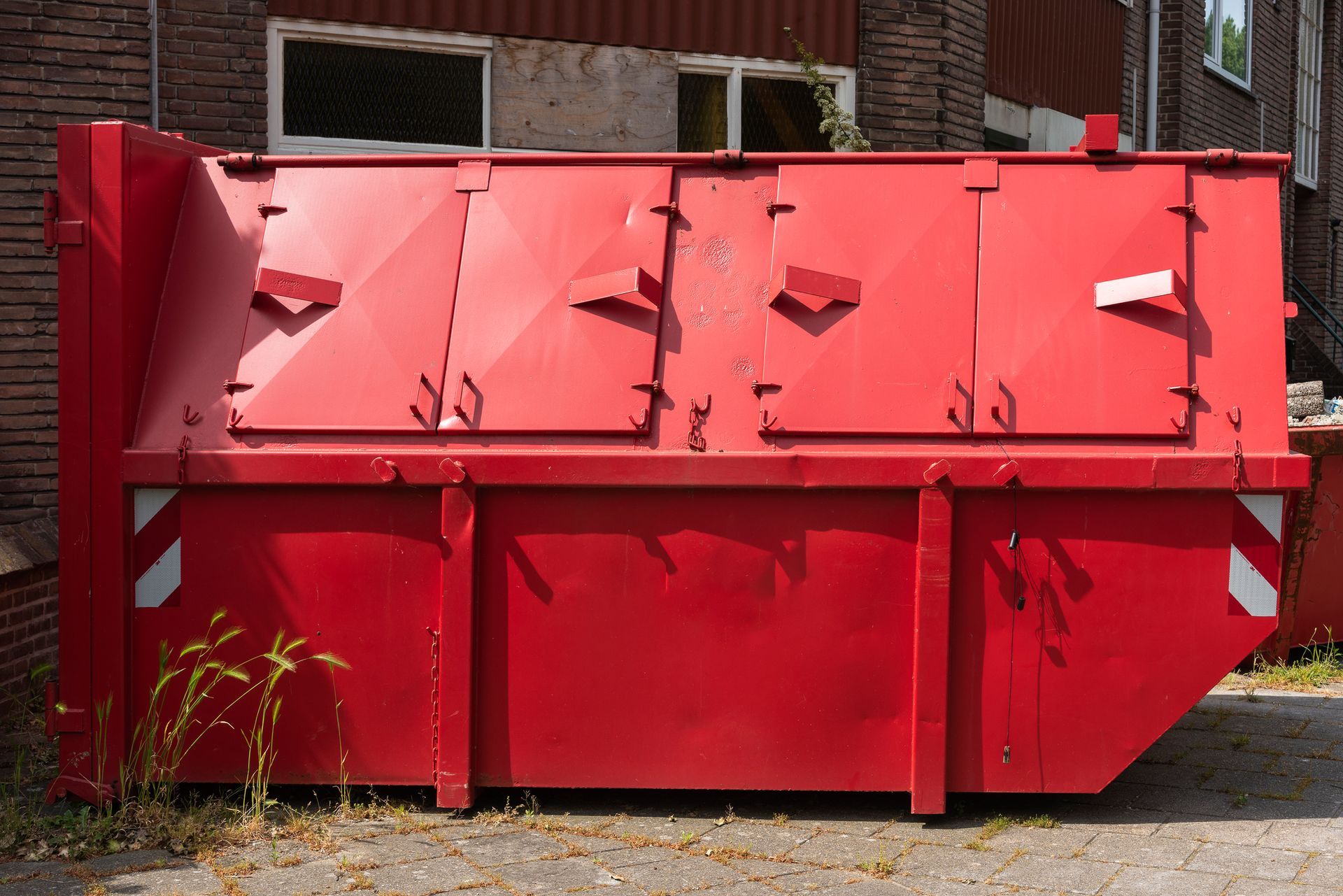 A red closed steel industrial waste container placed outside on the street in front of a house.
