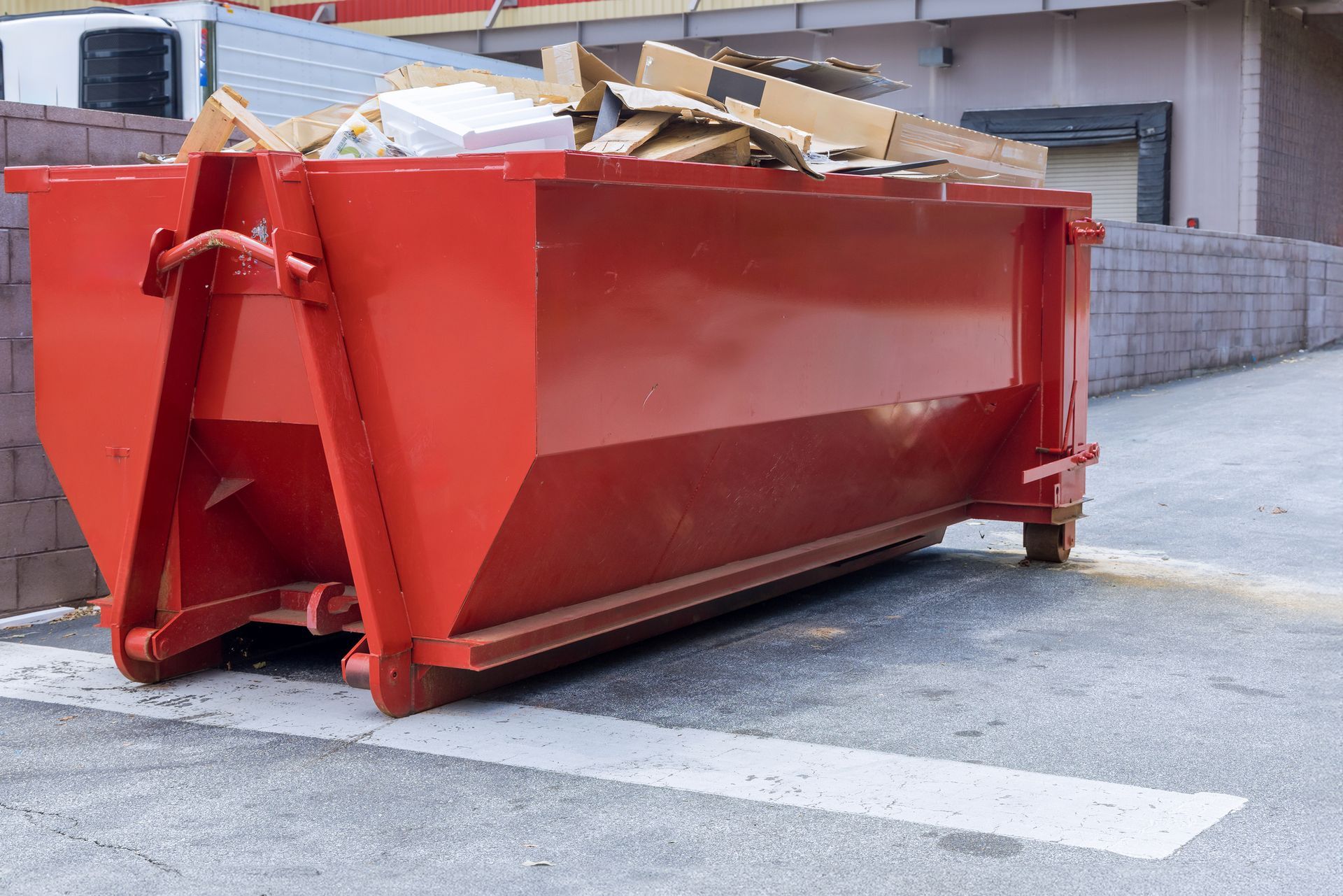 Red dumpster filled with cardboard and debris behind a commercial building.