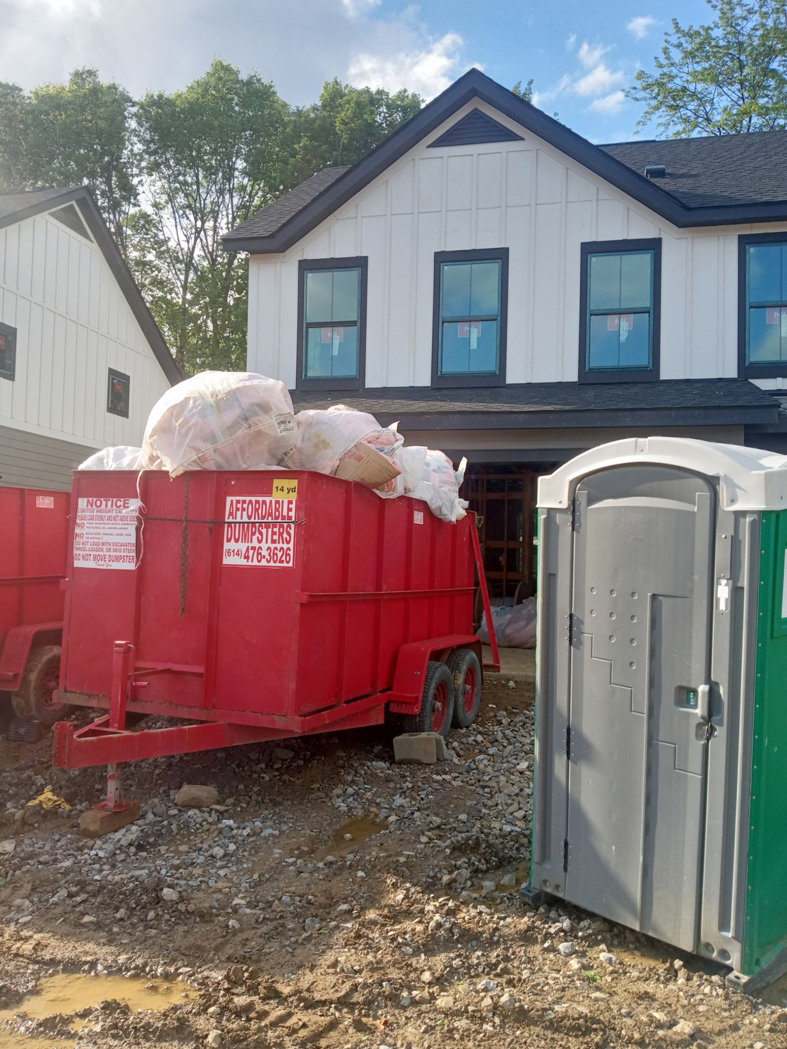 Red dumpster filled with white foam beside portable toilets at a muddy construction site.